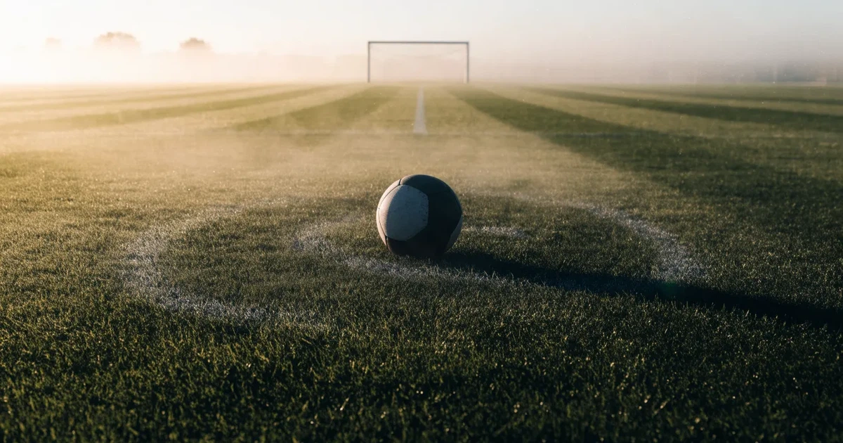 Uma bola de futebol no ponto central de um relvado, à luz da manhã